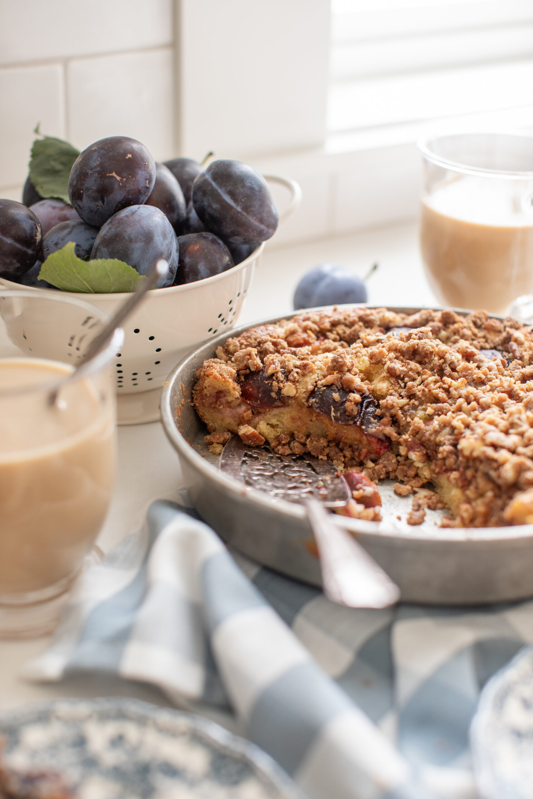 Plum coffee cake sliced with coffee and bowl of fresh plums