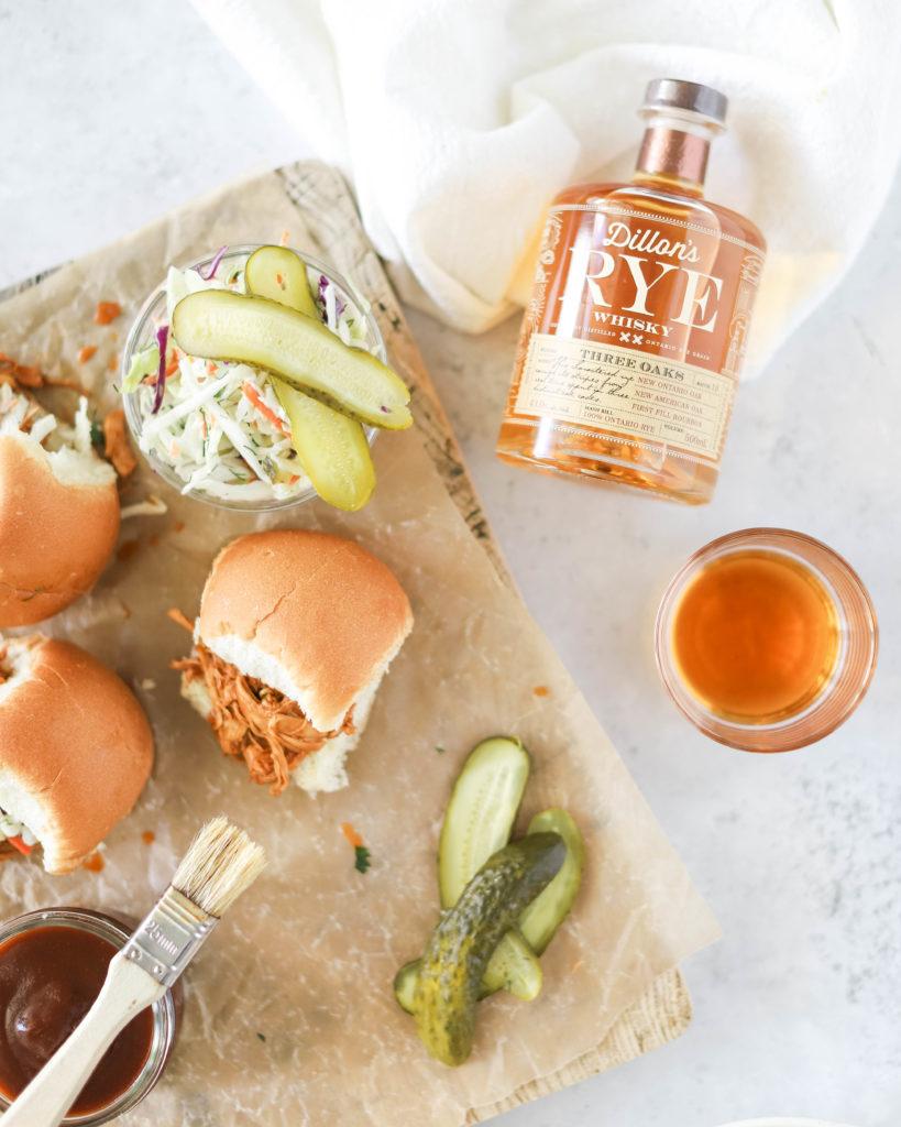Whiskey BBQ Chicken Crockpot Sliders on a board with pickles and bottle of whiskey