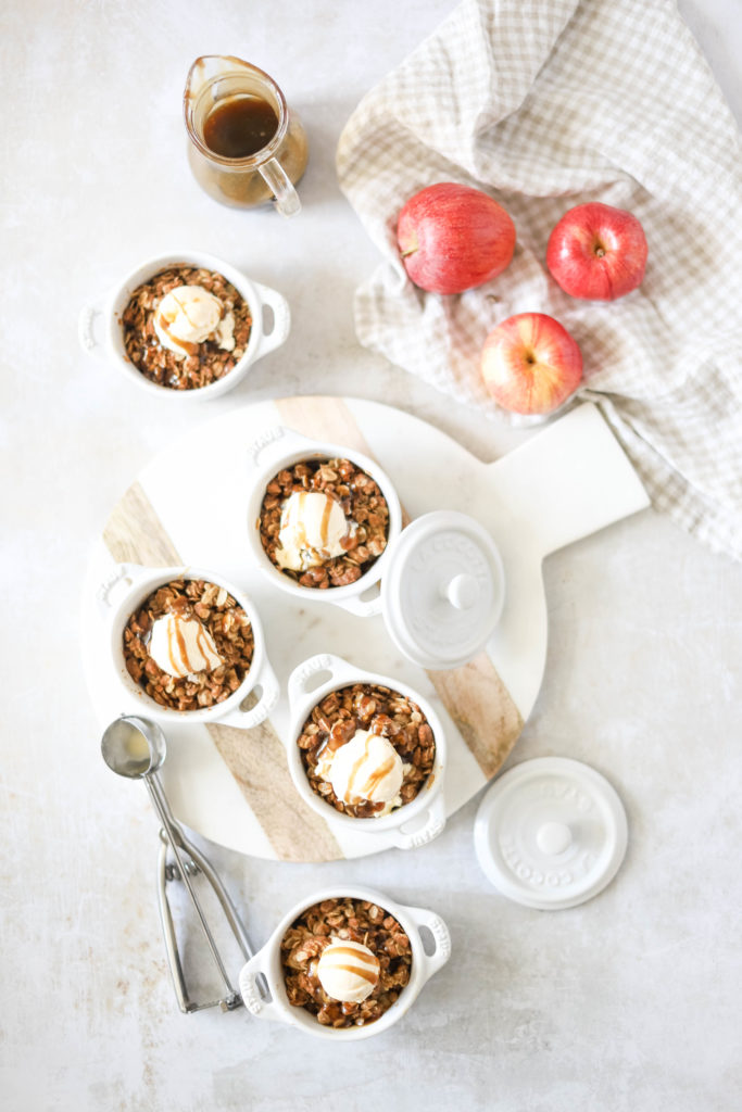 Beth’s Bourbon Apple Crisp in a white ramekin with a scoop of ice cream and caramel sauce drizzle