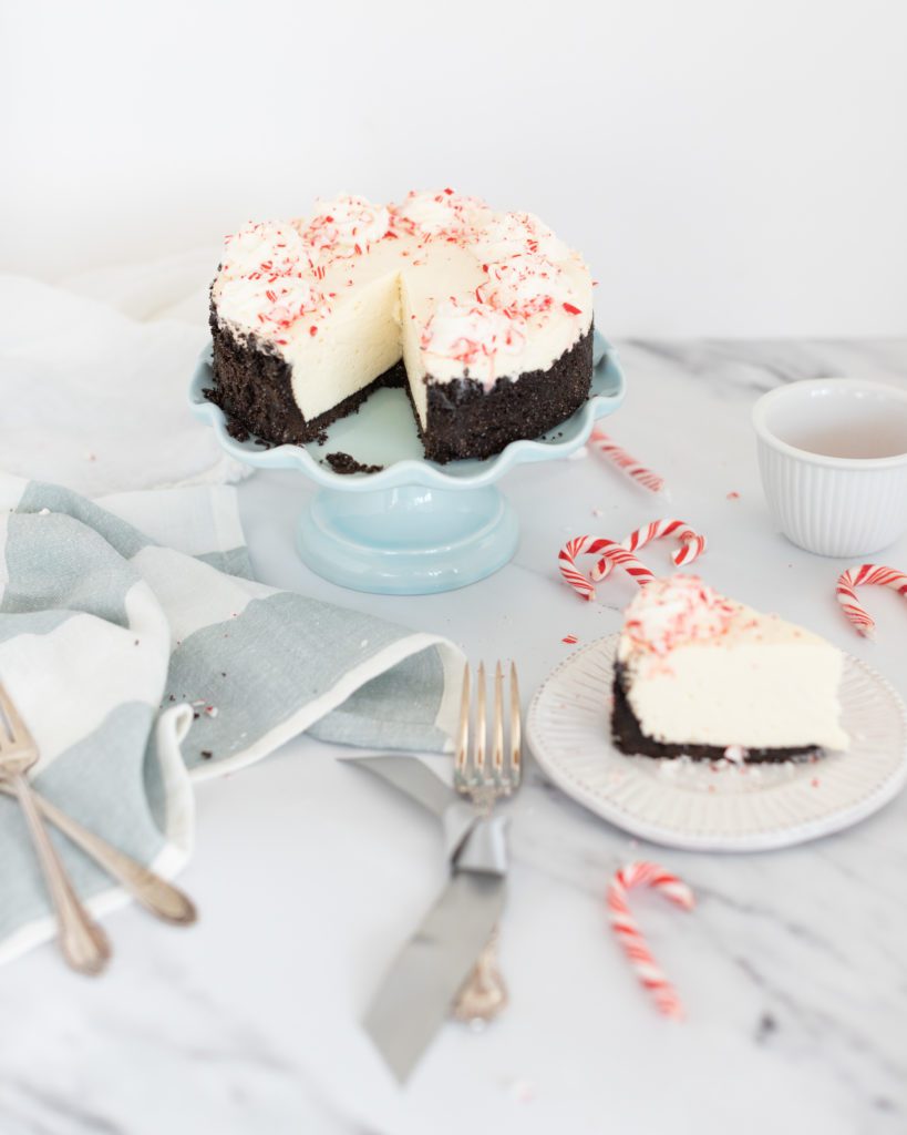 Homemade No Bake Peppermint Cheesecake by Fraiche Living on a blue cake stand topped with candy canes