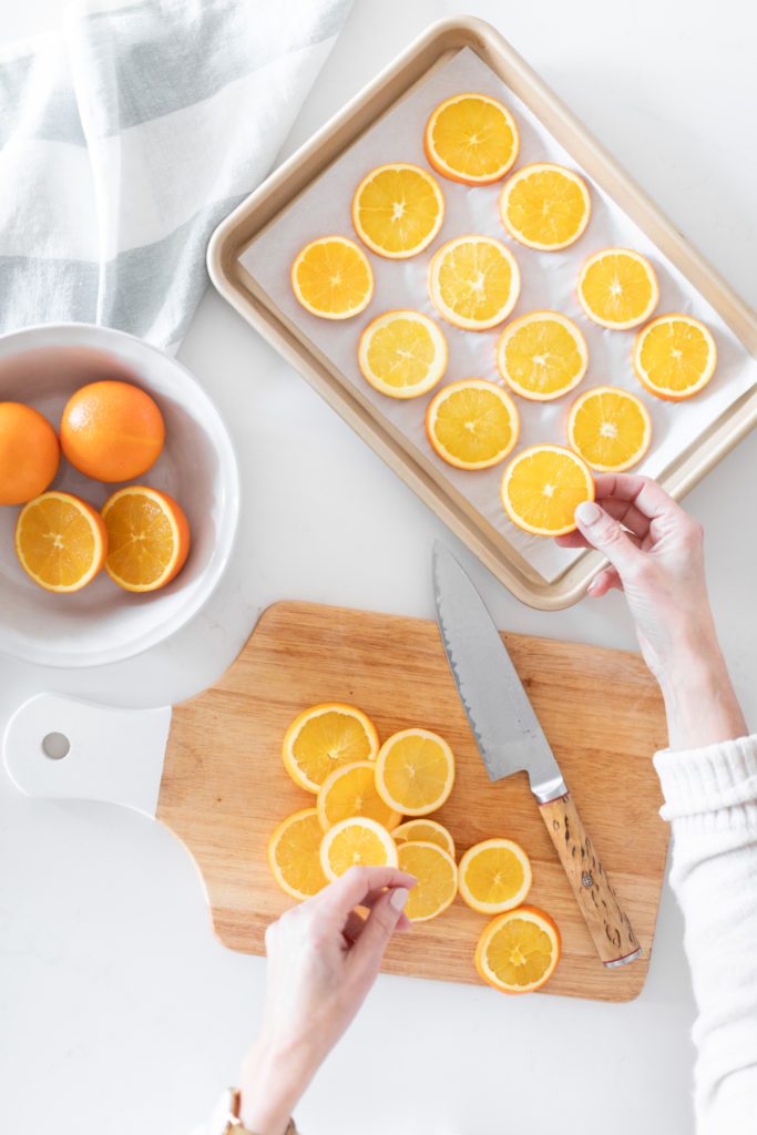 hand making dried orange slices on a baking sheet
