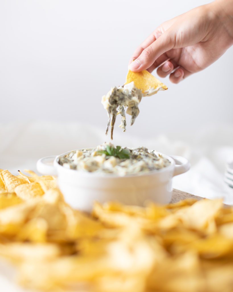 Hand grabbing chip with Crockpot Spinach and Artichoke Dip 