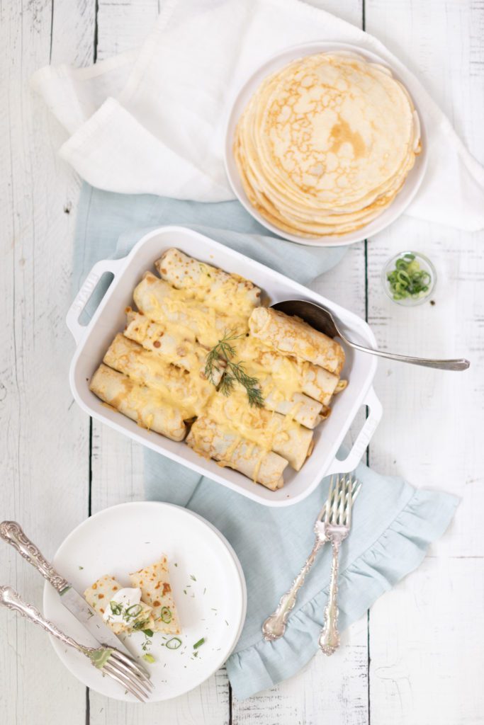 crepe casserole in a white baking dish topped with fresh dill and chives