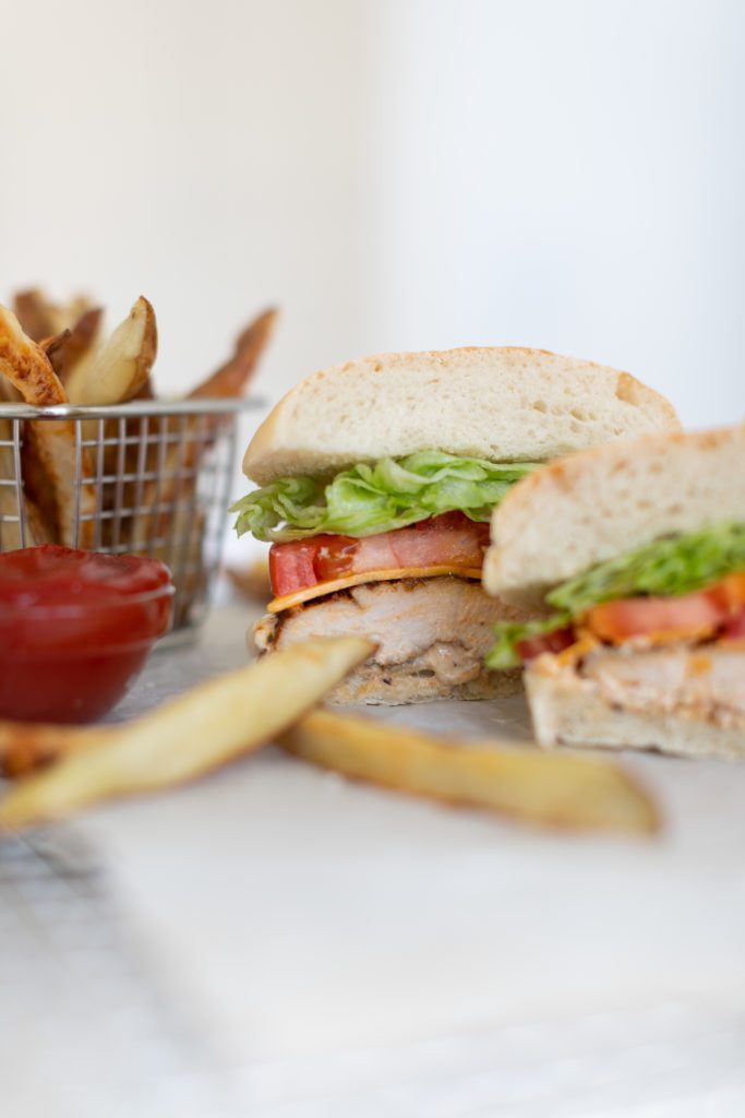 Fraiche Table  Cajun Chicken Sandwich cut in half with lettuce, tomato and cheese on a ciabatta bun with a side of fries