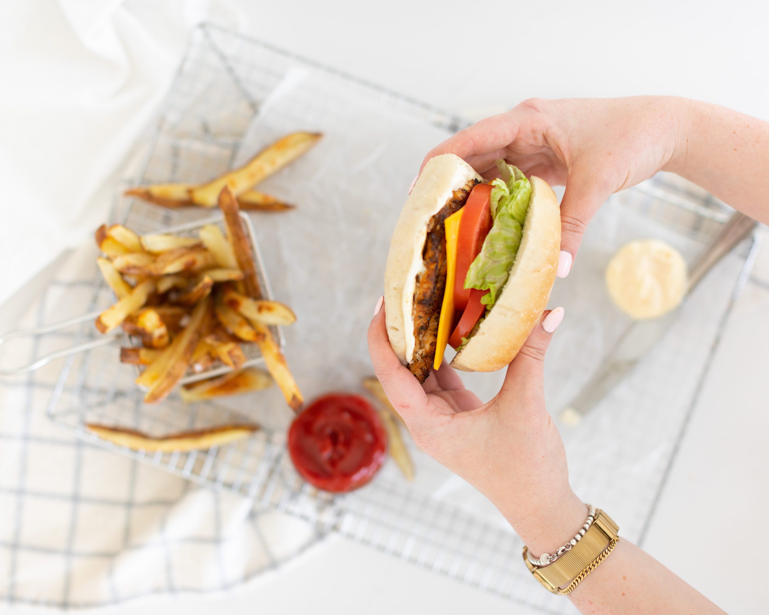 two hands holding up a Fraiche Table Cajun Chicken Sandwich with lettuce, tomato and cheese on a ciabatta bun with a side of fries