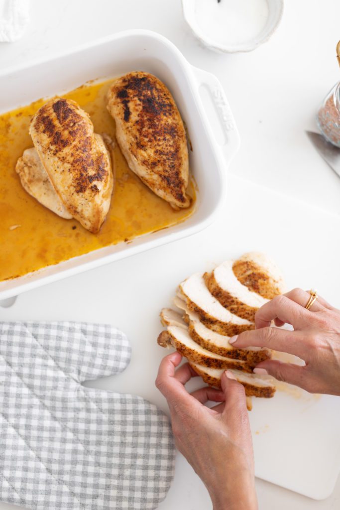 hand placing sliced chicken breast on a cutting board