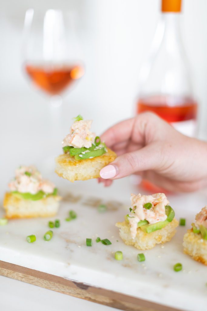 hand holding crispy rice with sweet and spicy shrimp appetizer with rose wine in the back