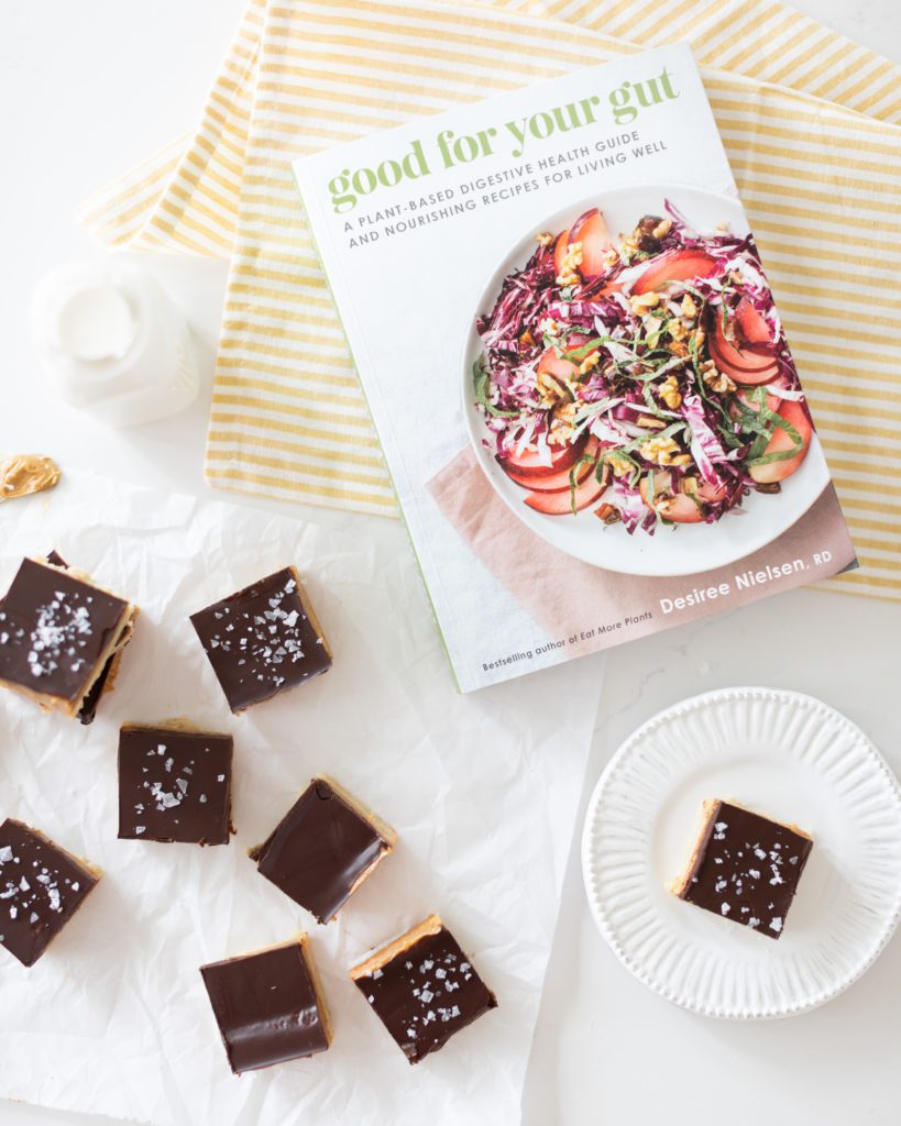 کتاب آشپزی خوب برای روده شما نوشته Desiree Bielson در کنار میله های شیرینی شکلاتی و کره بادام زمینی