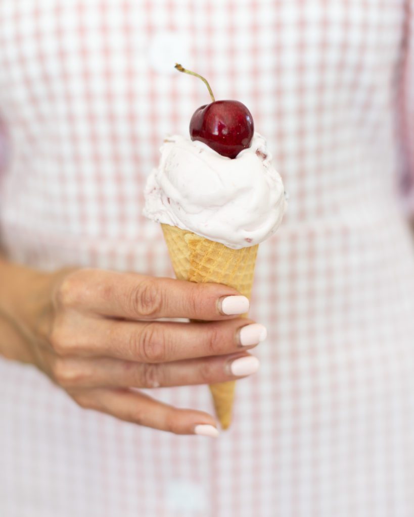homemade hand holding a cone of vanilla cherry ice cream