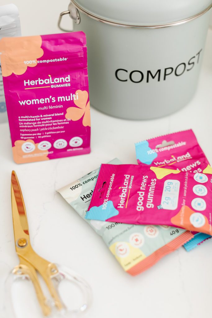 Herbaland Compostable Vitamin Gummies in pink packages beside a tabletop compost bin