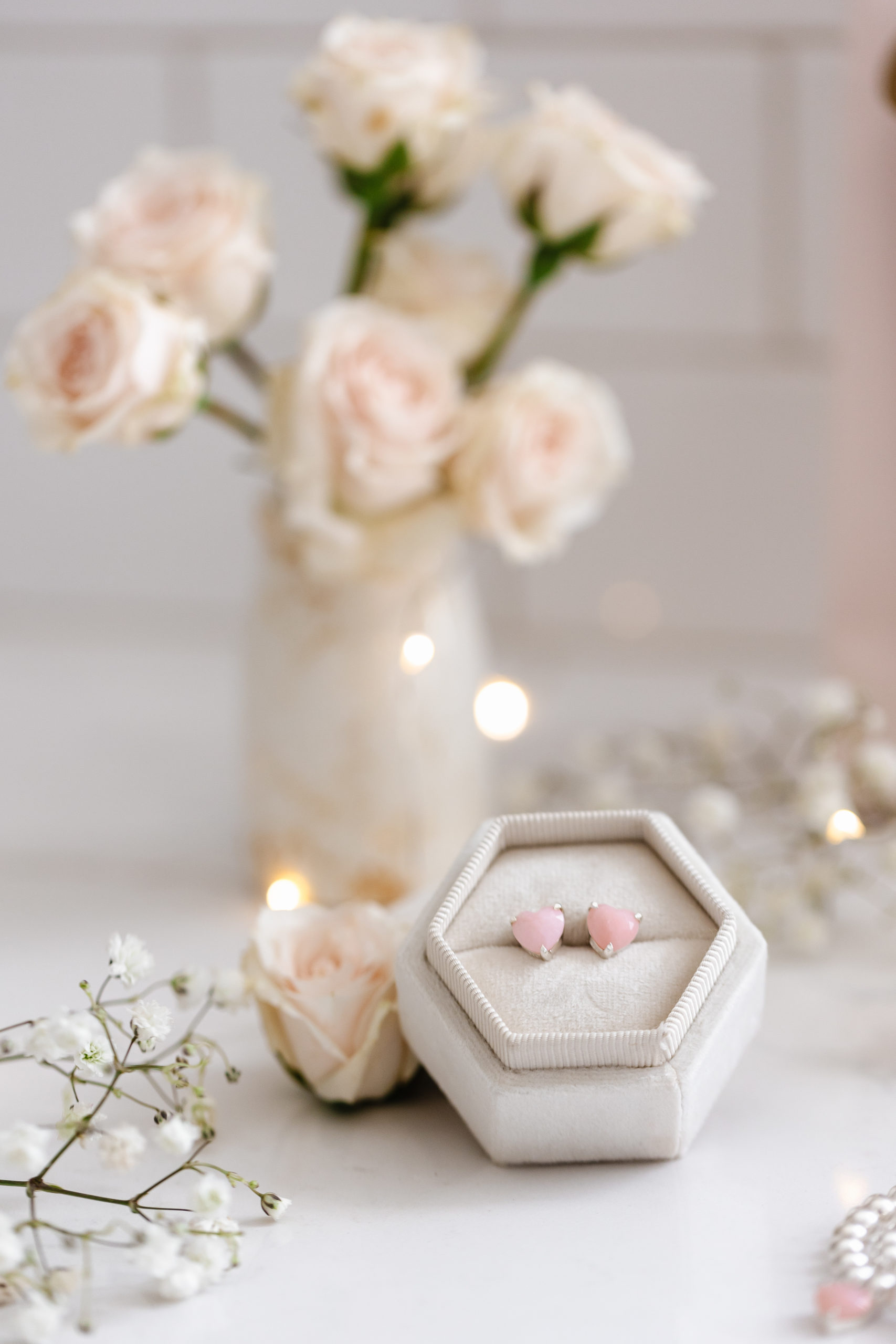 pink heart earrings in a box beside a vase of roses