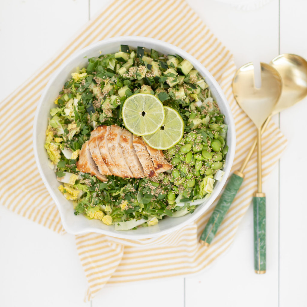 Fraiche Table Edamame crunch salad in a bowl topped with a sliced chicken breast and lime wedges