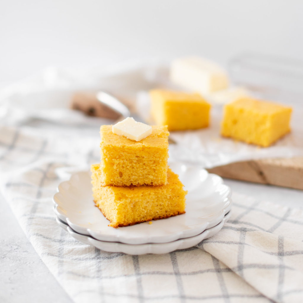 Old Fashioned Cornbread stacked on a plate with butter
