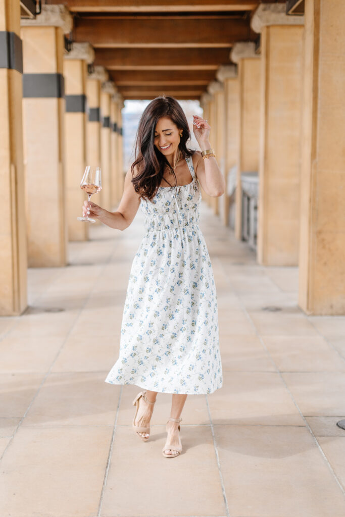Tori dancing in her blue and white floral dress with a glass of wine from The Fraîche x PRIV Summer Collection