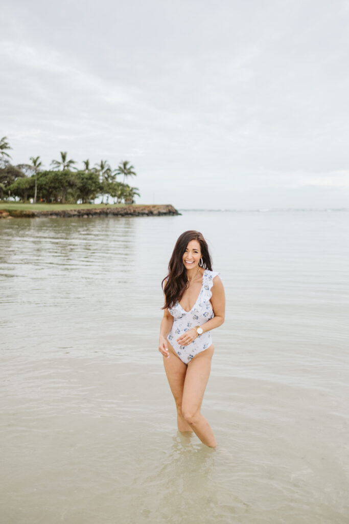Tori smiling I the shallow water of Hawaii in ruffle one-piece bathing suit from The Fraîche x PRIV Summer Collection
