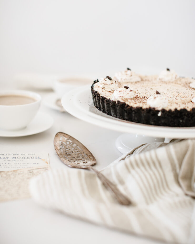 Café Au Lait Cheesecake on a cake stand with a cup of coffee