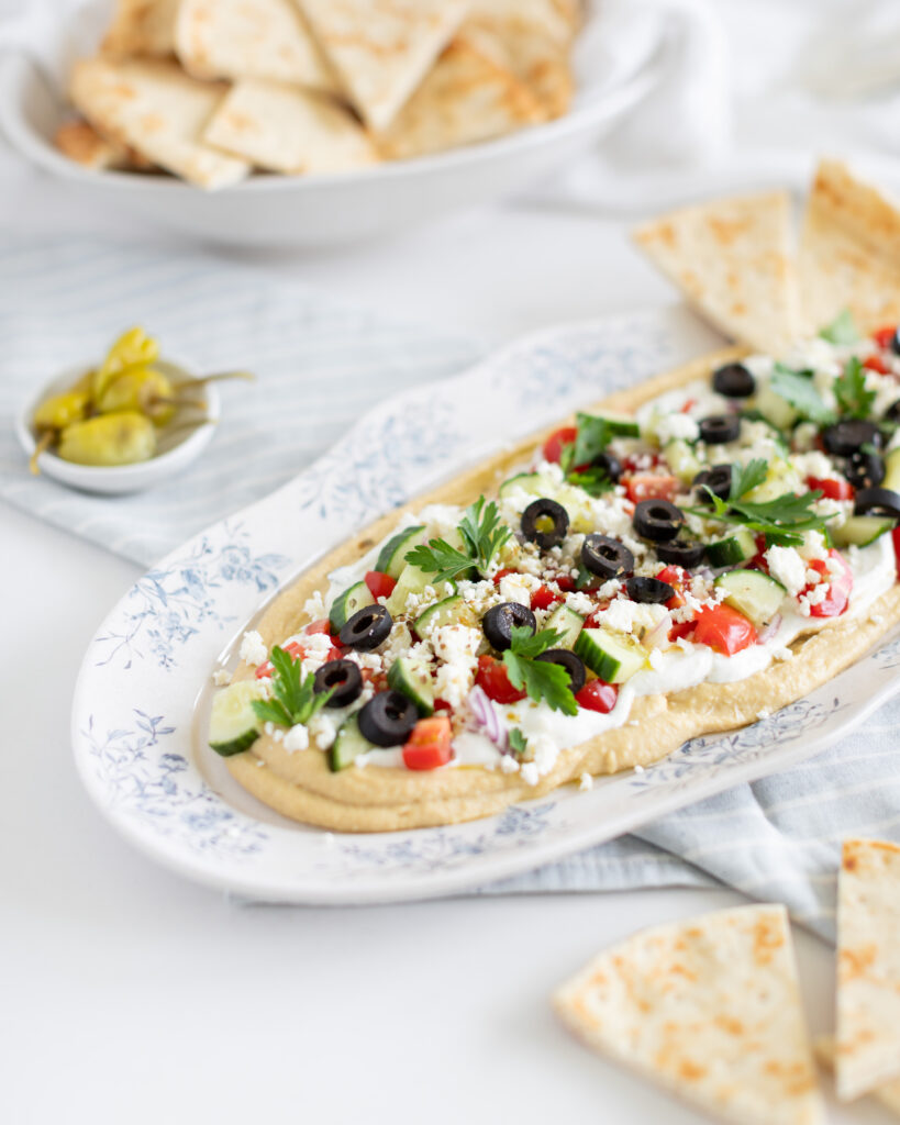 a 7-Layer Greek Dip with hummus, tzatziki, tomatoes, cucumbers, feta and olives, on a tray