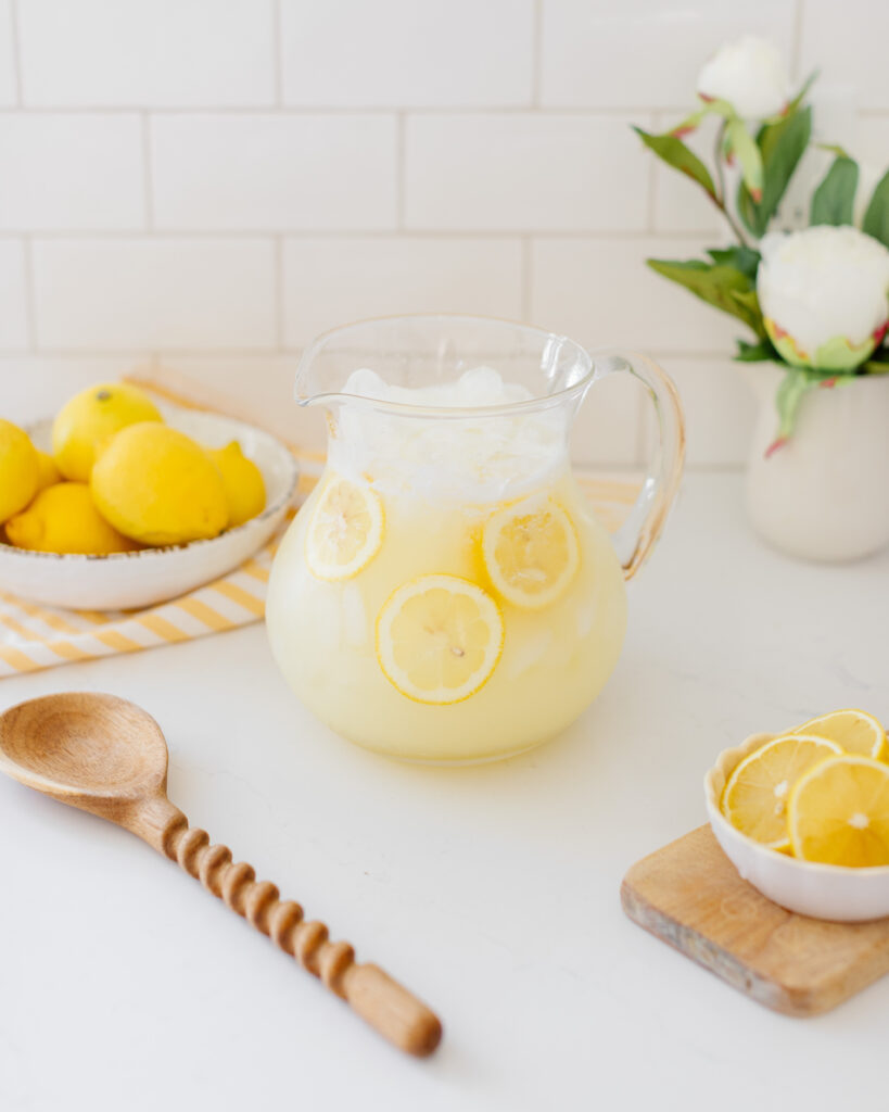 Homemade blender lemonade in a clear glass pitcher with lemon slices and ice