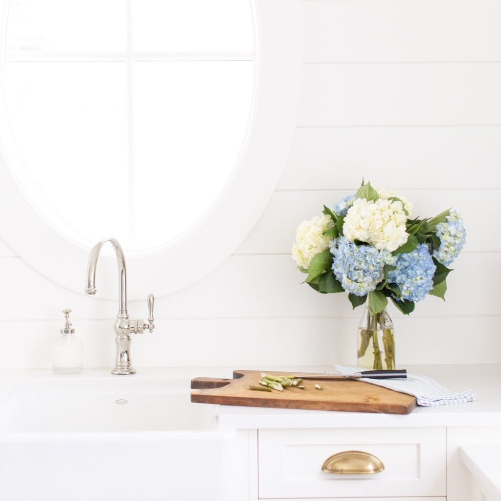 vase of blue and white hydrangeas, sitting next to a sink