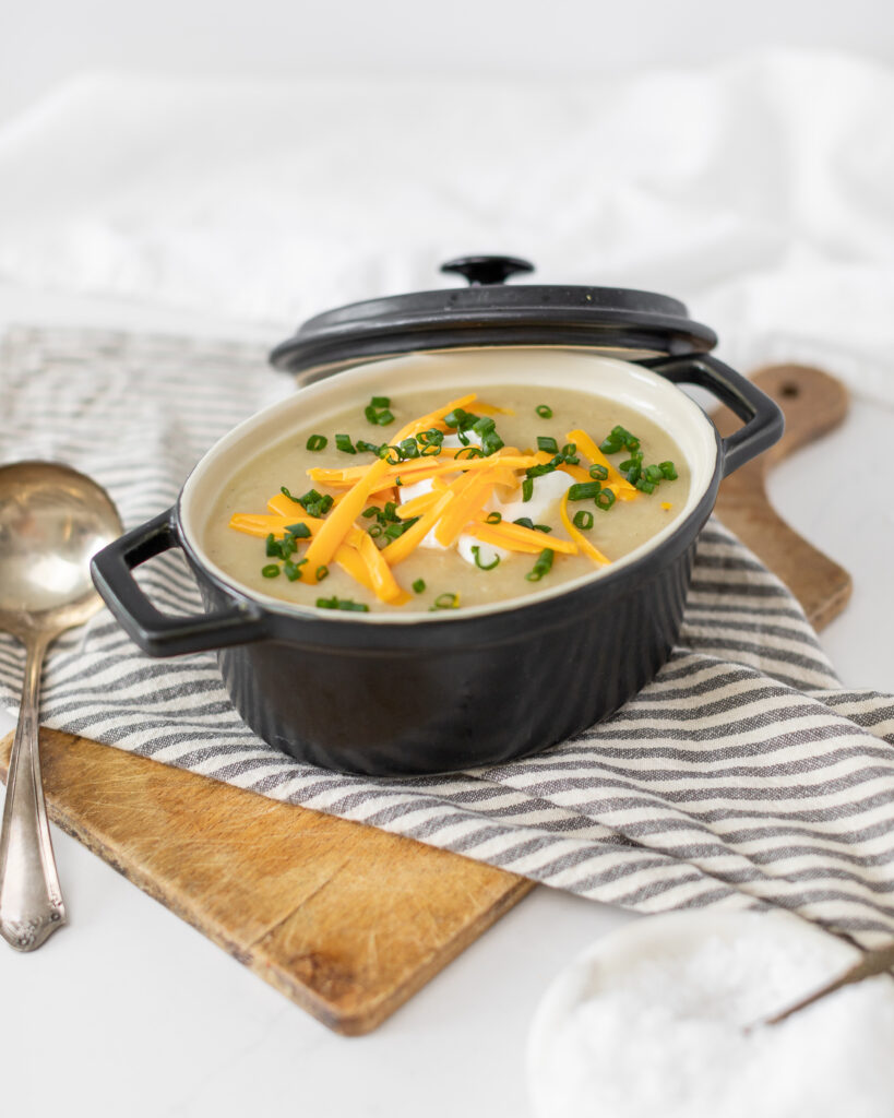 Slow Cooker Baked Potato Soup in a black pot topped with cheese and green onions