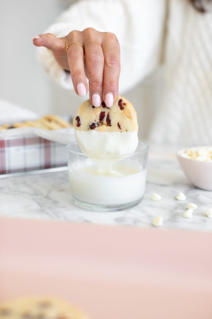 hand dunking Cranberry White Chocolate Slice & Bake Cookie in a cup of melted white chocolate