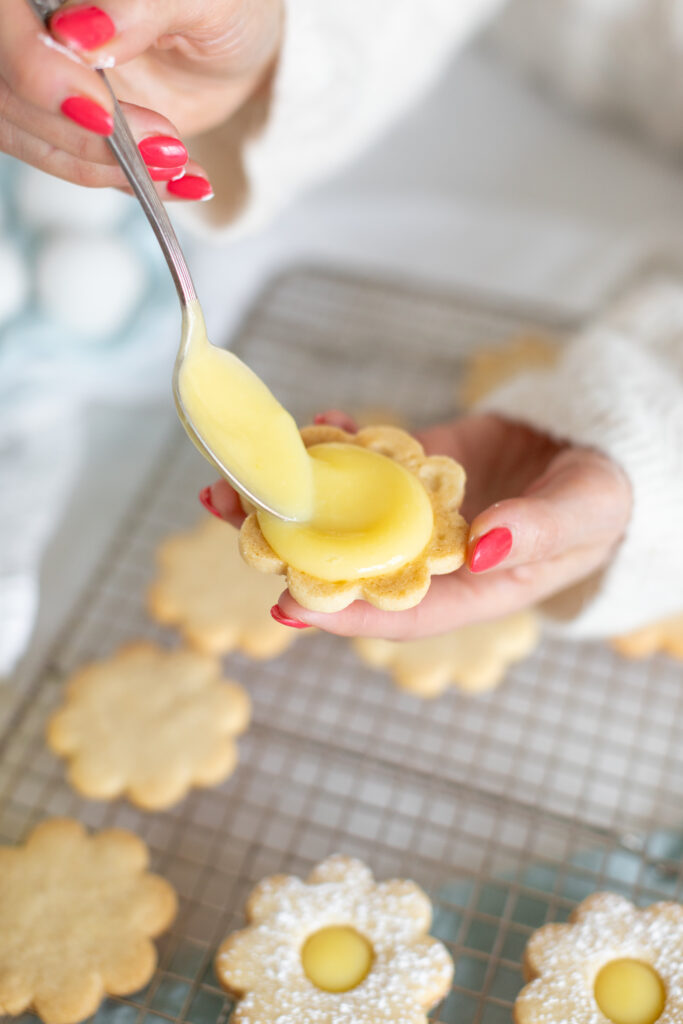 a hand filling a Lemon Cut-Out Cookie with lemon curd
