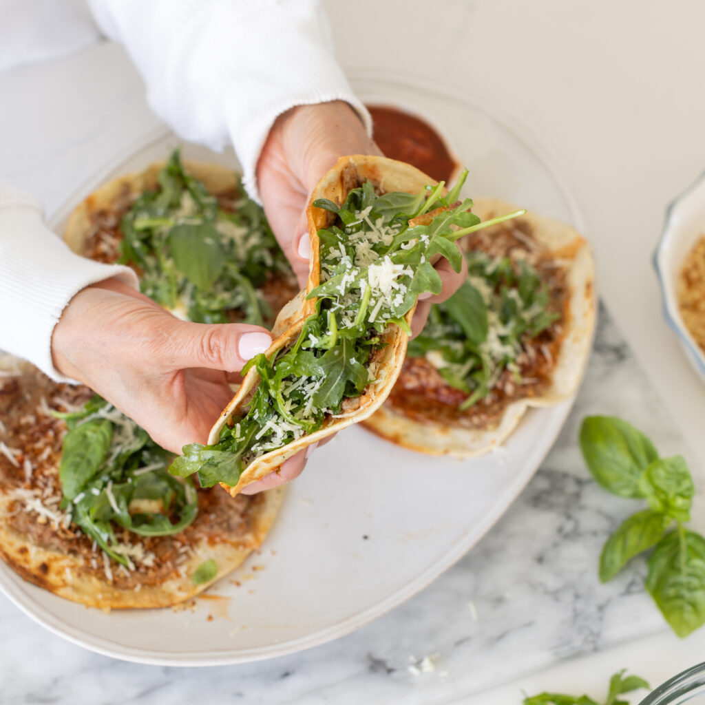 Hand holding a Chicken Parm Smash Tacos with arugula and parm cheese