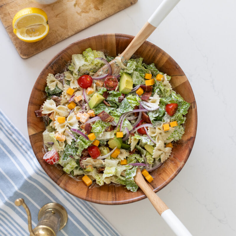 bowl of BLT pasta salad with bowtie pasta, crispy bacon, cherry tomatoes, cheddar cheese, romaine lettuce, red onion, avocado, and creamy ranch dressing