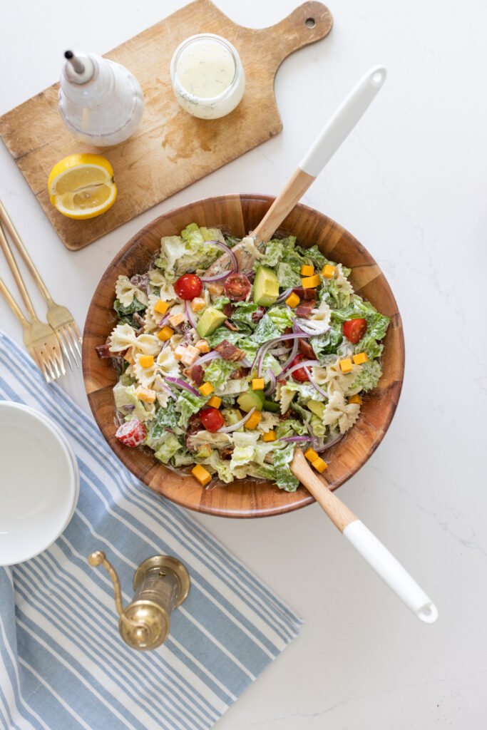large bowl pf BLT pasta salad with bowtie pasta, crispy bacon, creamy avocado, juicy tomatoes, cheddar cheese, and romaine lettuce, tossed in ranch dressing.