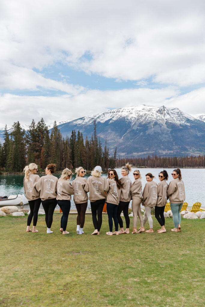 The bridal party posing outside the cabin at Fairmont Jasper Park Lodge during a Jasper bachelorette weekend in matching sweaters