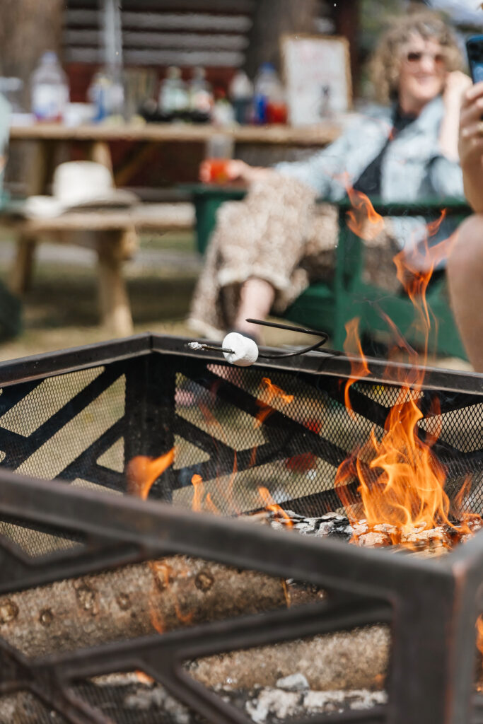 Outdoor fire pit scene with friends roasting marshmallows, making Caesars, and relaxing during a mountain bachelorette weekend in Jasper.