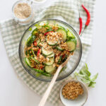 Bowl of spicy cucumber salad garnished with fresh mint, crushed peanuts and chilis