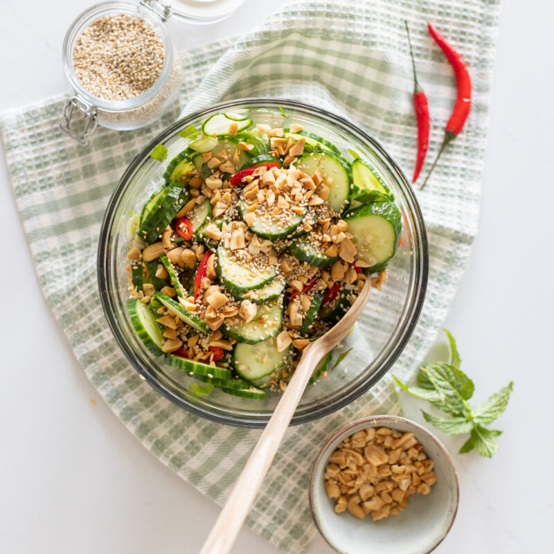 Bowl of spicy cucumber salad garnished with fresh mint, crushed peanuts and chilis
