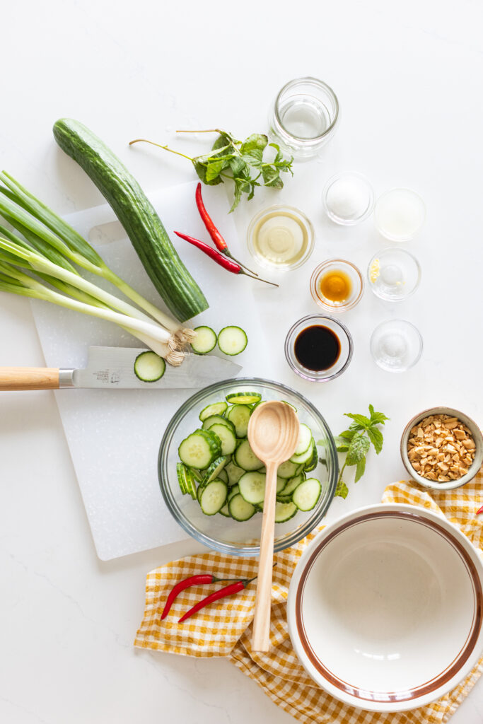 Flat lay of ingredients for spicy cucumber salad including cucumbers, lime, chilis, soy sauce, and mint