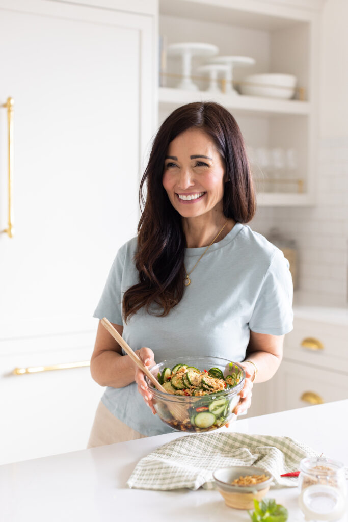 Tori holding bowl spicy cucumber salad garnished with fresh mint and crushed peanuts