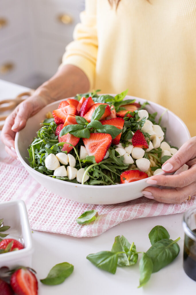 Strawberry Caprese Pasta Salad in a serving bowl, topped with fresh basil, sliced strawberries, and halved bocconcini.