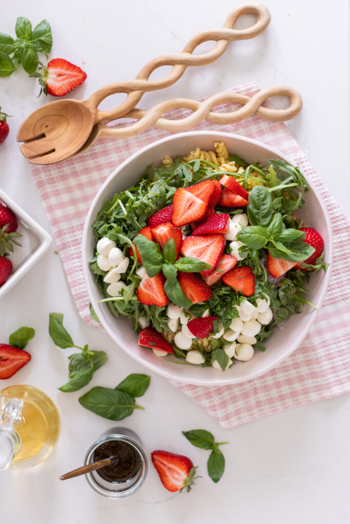 Strawberry Caprese Pasta Salad in a serving bowl, topped with fresh basil, sliced strawberries, and halved bocconcini.