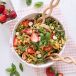 Strawberry Caprese Pasta Salad in a serving bowl, topped with fresh basil, sliced strawberries, and halved bocconcini.