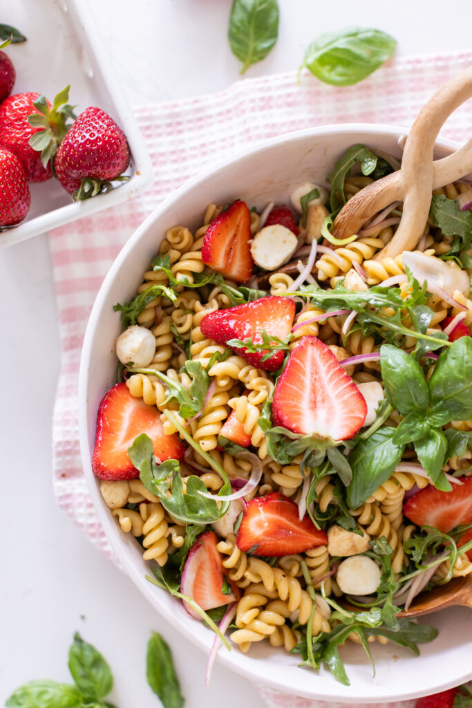 Strawberry Caprese Pasta Salad in a serving bowl, topped with fresh basil, sliced strawberries, and halved bocconcini.