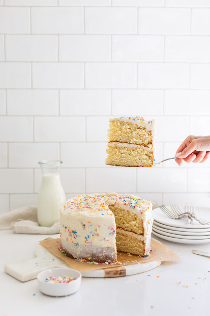 The Perfect Vanilla Cake decorated with colourful sprinkles on top, one slice taken out 