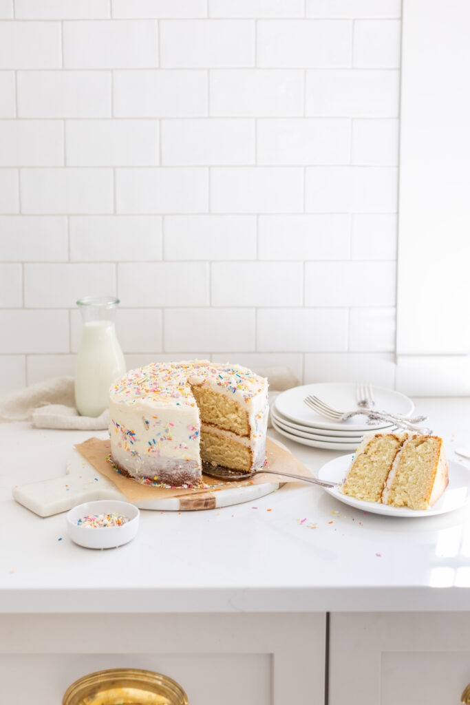The Perfect Vanilla Cake decorated with colourful sprinkles on top, one slice taken out 