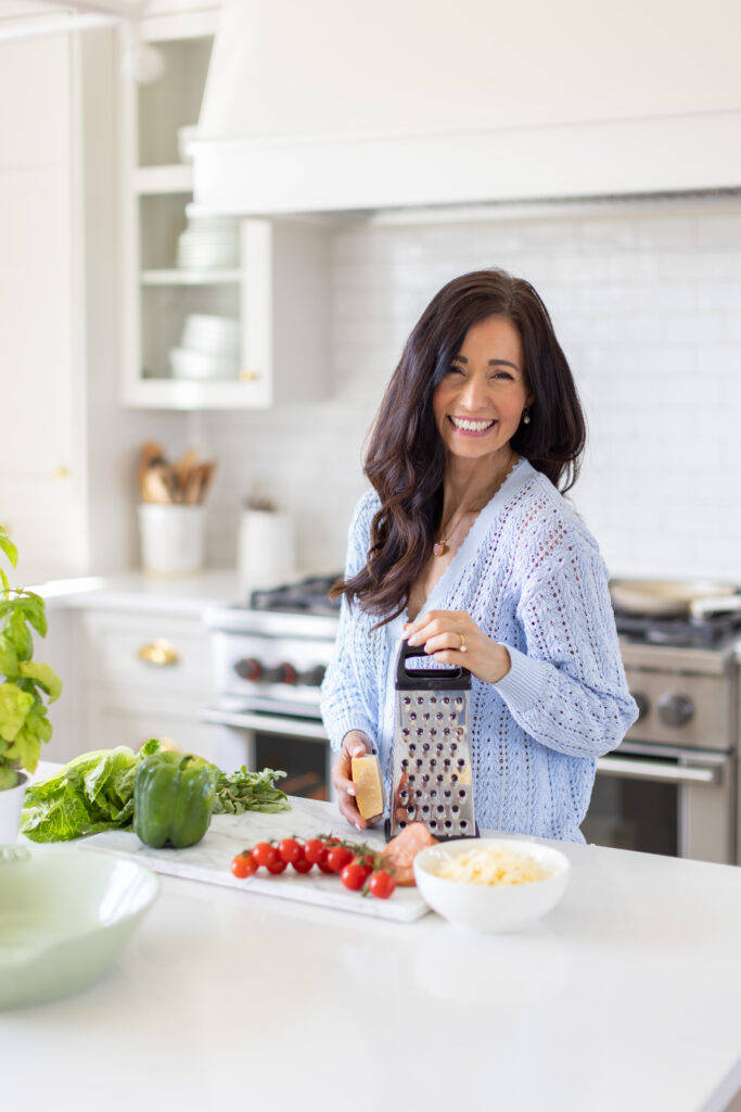 Tori grating cheese while prepping Pizza Ranch Salad in a bright, modern kitchen.