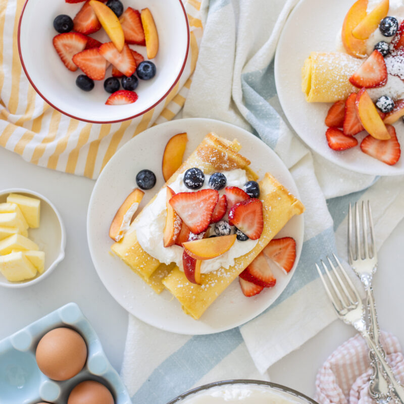 Sheet pan crepes topped with fresh strawberries, blueberries, and whipped cream, served on a white plate for an easy breakfast.