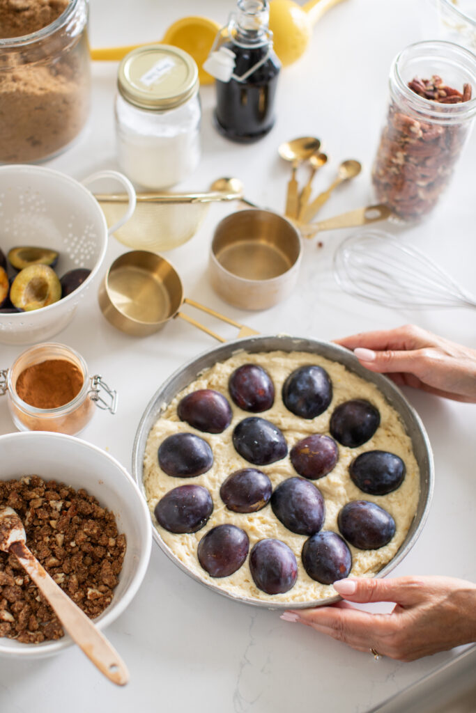 Close-up of halved Italian plums being placed into the cake batter before baking.