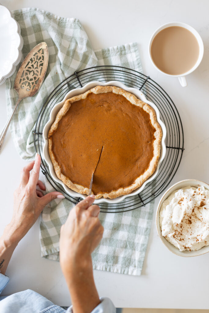 The best pumpkin pie in a white pie plate on a cooling rack, Tori cutting into it.