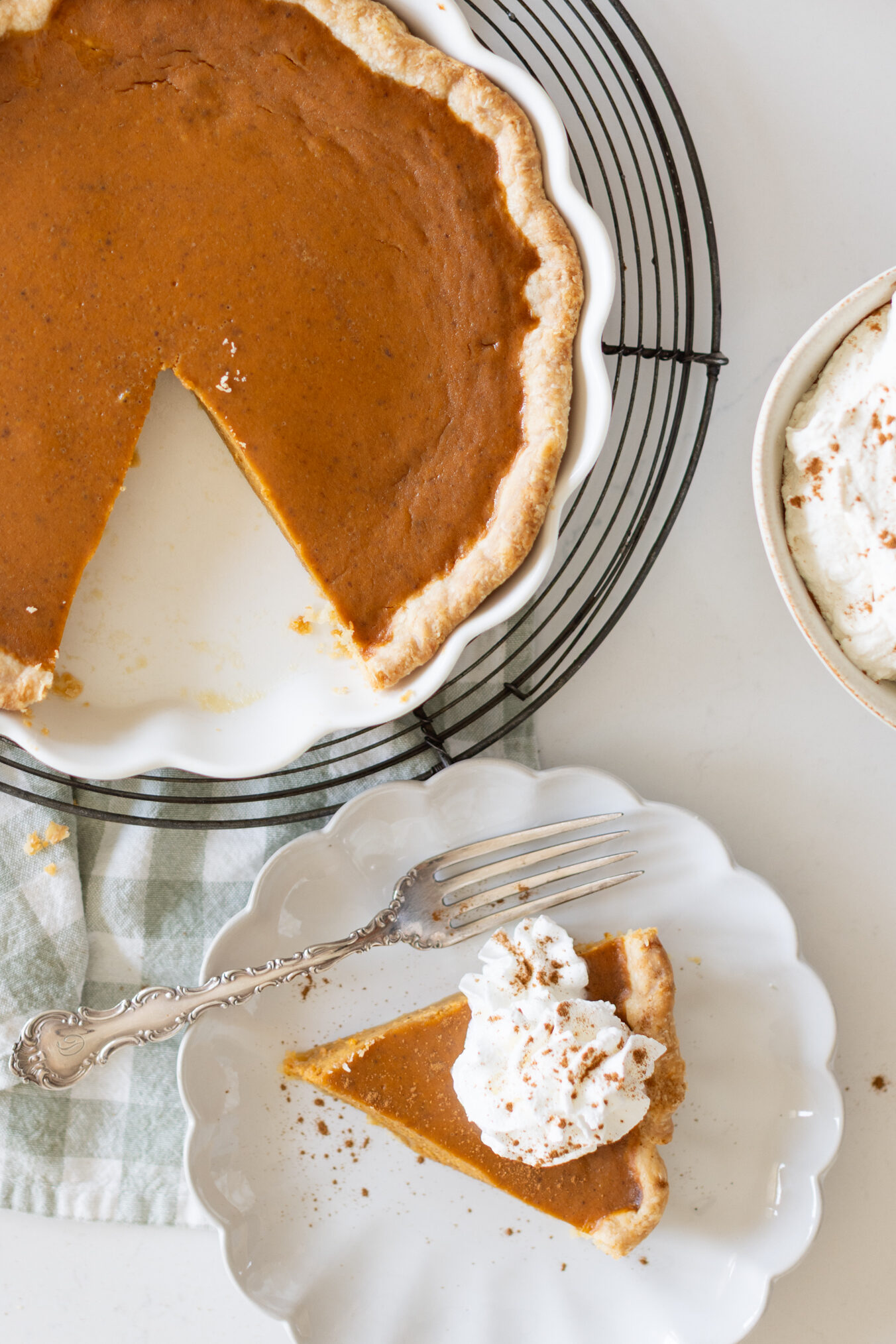 Best pumpkin pie in a white pie dish with one slice removed, slice on a plate topped with Chantilly Cream, served with coffee on a fall table.