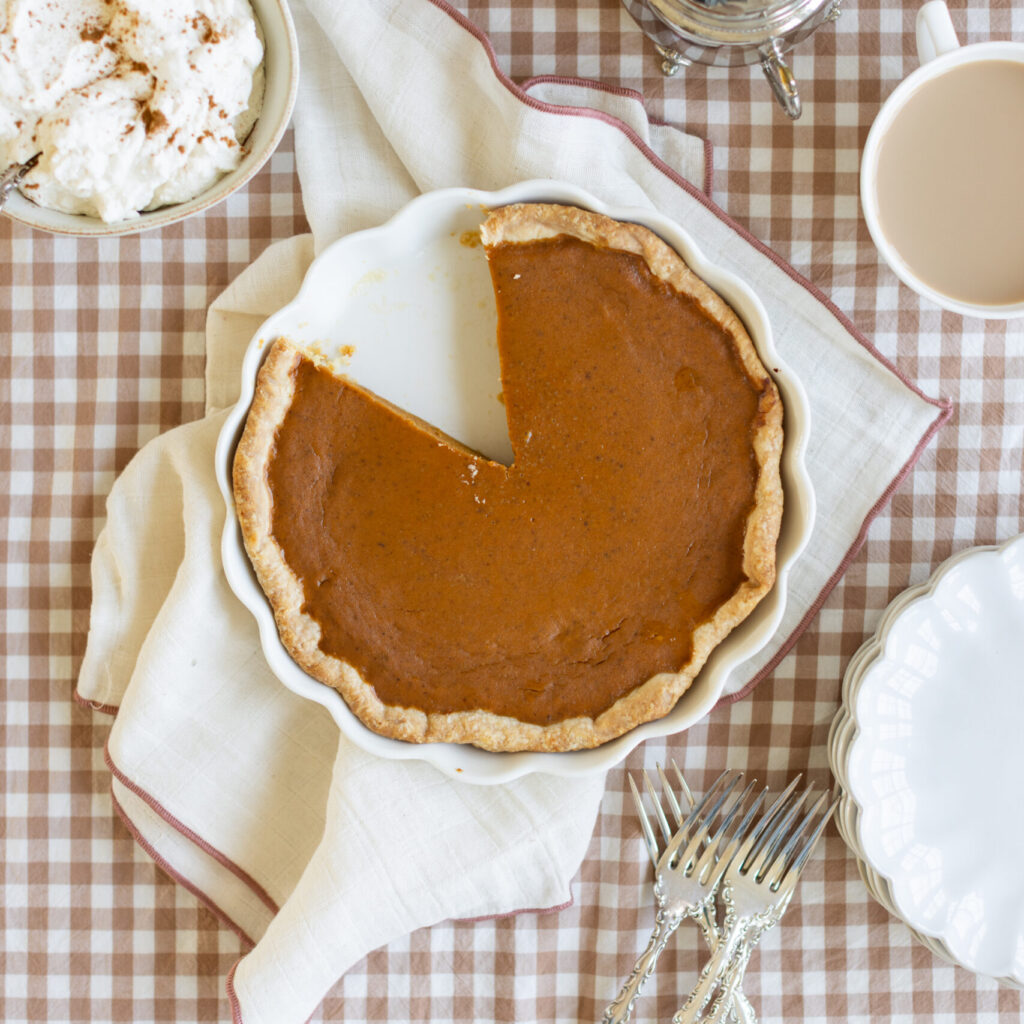 The best pumpkin pie in a white pie plate with one slice removed, served on a decorated Thanksgiving table.